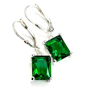 May include: A pair of silver leverback earrings with emerald-cut, vibrant green gemstones. The earrings have a rectangular shape and are set in a silver metal. The gemstones are a deep, rich green color, and the earrings are displayed against a white background.