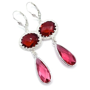May include: A pair of silver-toned drop earrings featuring a faceted oval-shaped deep red stone set in a rope-textured frame, connected to a faceted teardrop-shaped pink stone. The earrings are secured with silver-toned lever-back closures.