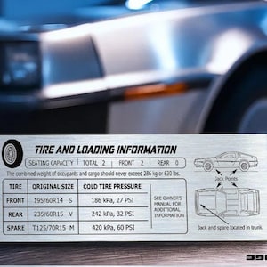 Peut inclure: Panneau en métal brossé avec des informations sur les pneus et le chargement, y compris les dimensions des pneus et la pression des pneus à froid en kPa et PSI. Le fond montre une voiture argentée.