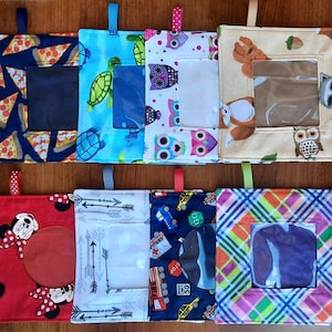 May include: Eight square fabric pouches with hanging loops, each featuring a clear plastic window. Patterns include pizza slices, turtles, colorful owls, woodland animals, cartoon mice, arrows, city traffic signs, and a multi-colored plaid design.