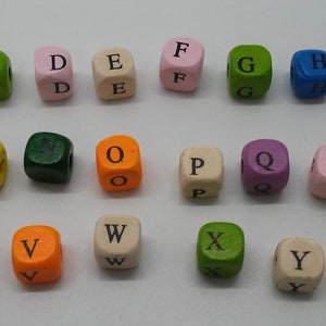 Puede incluir: Una colecci&oacute;n de veintis&eacute;is cuentas de madera cuadradas, cada una con una letra negra del alfabeto de la A a la Z. Las cuentas est&aacute;n pintadas en varios colores, incluyendo morado, blanco, verde, rosa, azul, rojo, naranja y amarillo.
