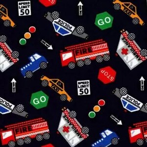 May include: A black fabric featuring a repeating pattern of emergency vehicles including red fire trucks, white ambulances, blue trucks, and yellow taxis. The design includes traffic signs reading Speed Limit 50, Stop, Go, and One Way arrows.