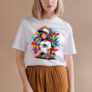 May include: White t-shirt featuring a colorful graphic of a cartoon skater girl with blue hair, a white cap, and headphones. The graphic includes a skateboard and vibrant paint splatters in shades of blue, yellow, orange, and red.