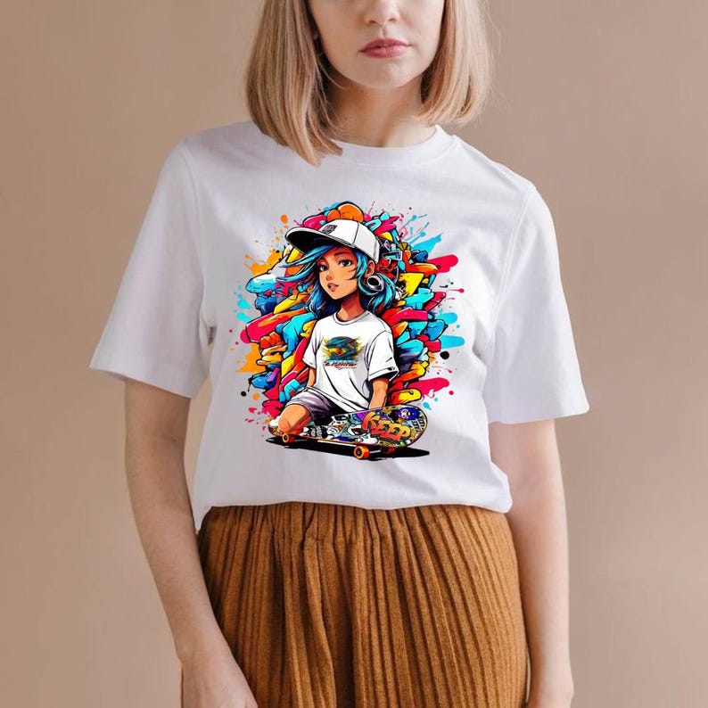 May include: White t-shirt featuring a colorful graphic of a cartoon skater girl with blue hair, a white cap, and headphones. The graphic includes a skateboard and vibrant paint splatters in shades of blue, yellow, orange, and red.