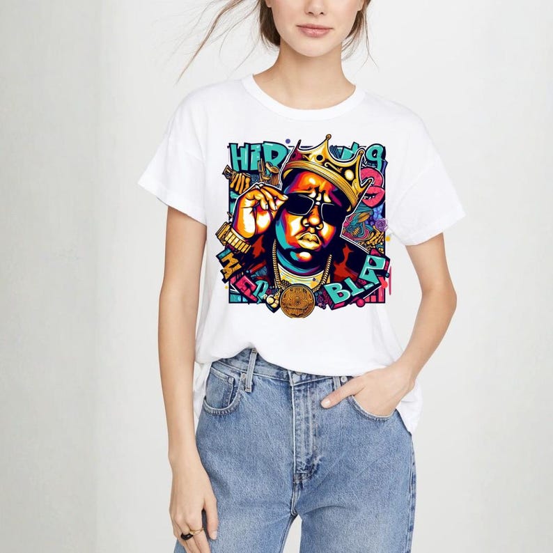 May include: White t-shirt featuring a colorful graphic of a person wearing sunglasses and a gold crown. The graphic includes the text "HIP" and "BLP". The person is wearing gold jewelry and a gold medallion.