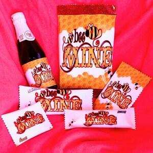 May include: A set of Valentine's Day themed gifts featuring a bottle of sparkling wine, a bag of candy, and several chocolate bars. Each item has a bee and the text "bee mine" printed on it.