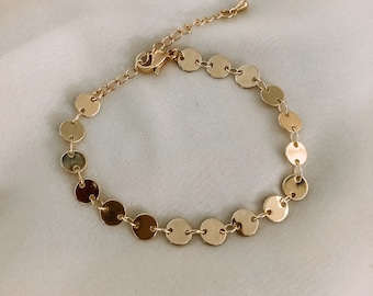 May include: A gold chain bracelet with a series of small, round, gold discs.
