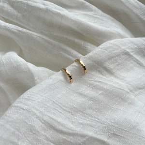 May include: A pair of gold hoop earrings with a textured, slightly bumpy surface.