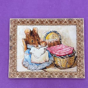 May include: A framed illustration of a brown mouse holding a baby mouse in a blue and white dress. The baby mouse is in a wicker basket with a pink blanket. The illustration is set against a white background.