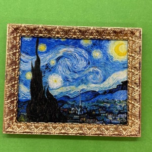 May include: A framed print of Vincent van Gogh's "Starry Night" painting. The painting depicts a swirling night sky with a bright yellow moon and stars. A dark cypress tree stands in the foreground, with a small village in the distance.