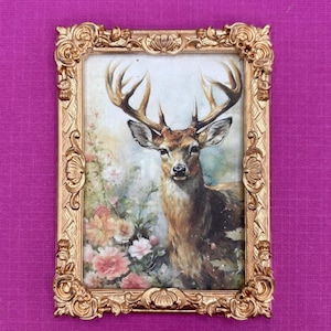 May include: A framed print featuring a majestic deer with large antlers, set against a backdrop of flowers. The frame is ornate, with a gold finish. The artwork has a vintage aesthetic, with soft colors and detailed brushstrokes.