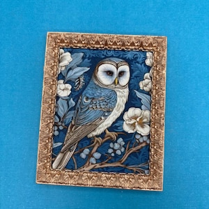 May include: A framed artwork featuring a blue and white owl perched on a branch, set against a dark blue floral background. The frame is gold-colored. The artwork has a vintage aesthetic.