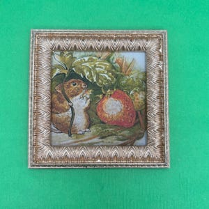 May include: A framed illustration of a small brown mouse eating a strawberry. The artwork is set against a backdrop of green leaves and a red strawberry. The frame is a decorative gold color.