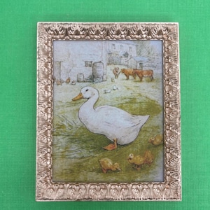 May include: A framed painting of a white duck with ducklings in a farmyard setting. The painting is in a gold frame with a decorative border.