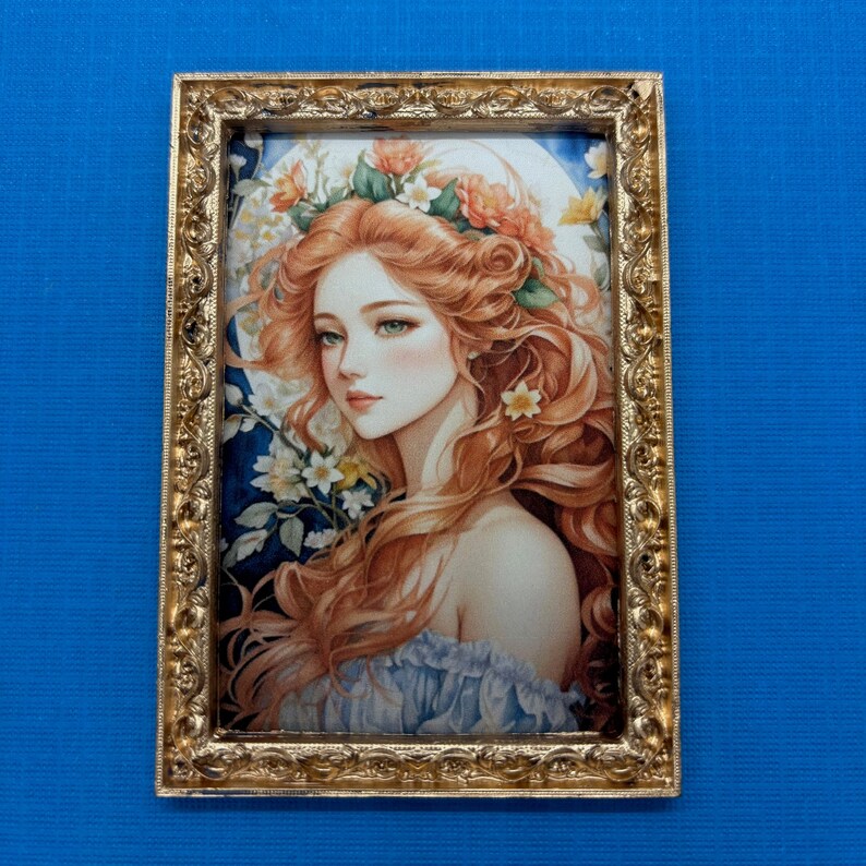 May include: A framed illustration of a woman with long, flowing red hair wearing a floral crown. She is depicted with a soft, ethereal expression and is surrounded by delicate flowers. The frame is ornate and gold.