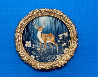 Peut inclure: Une image encadrée dorée d'un cerf debout dans une forêt avec des fleurs blanches. Le cerf est brun avec des taches blanches et a de grands bois.