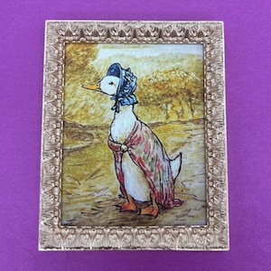 May include: A framed illustration of a duck wearing a blue bonnet and a pink and white shawl. The duck is standing in a field with trees in the background.