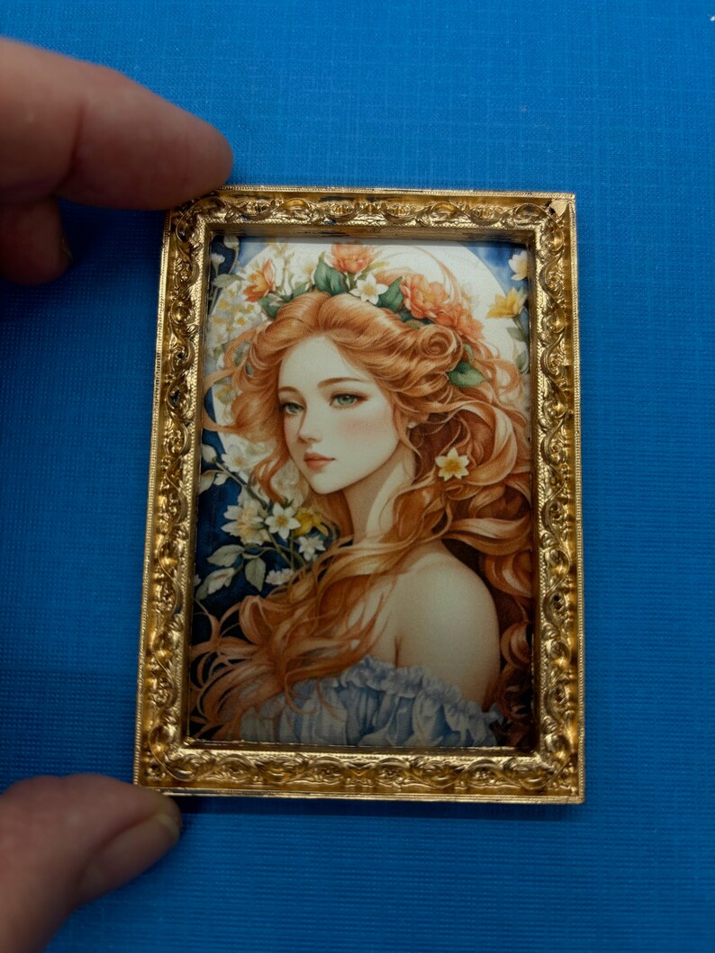 May include: A framed illustration of a woman with long, flowing red hair wearing a floral crown. The background is a blue and green watercolour wash with white flowers.