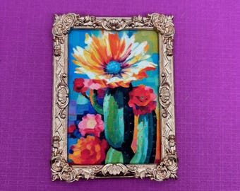 May include: A framed painting of a colourful cactus flower with a yellow, orange and white flower and green cactus stems. The frame is gold and ornate.