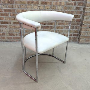 May include: A white leather chair with a curved back and seat, supported by a chrome frame. The chair has a modern design and is set against a brick wall.