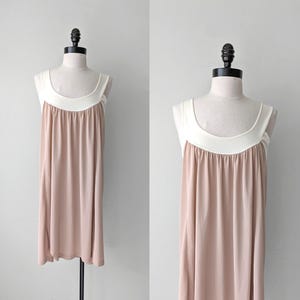 May include: A vintage-style, sleeveless dress in a soft, neutral color, displayed on a mannequin. The dress features a contrasting white neckline and a flowing, knee-length skirt. The fabric drapes elegantly, suggesting a lightweight material.