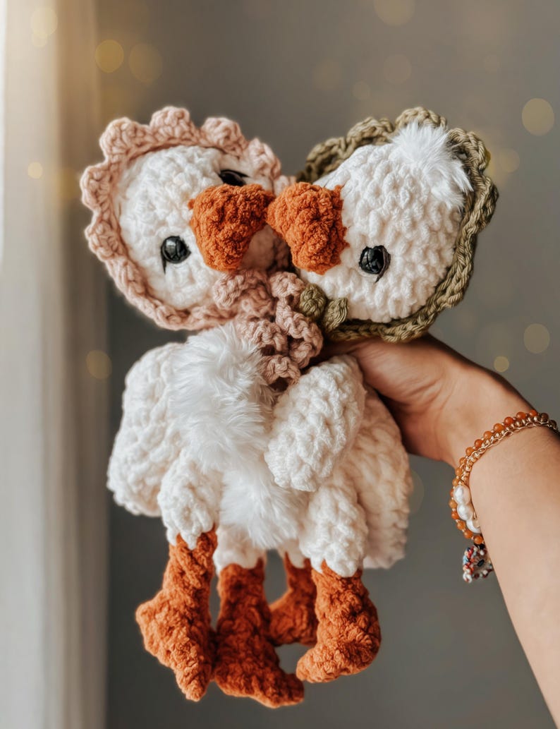 Pu&ograve; includere: Due peluche di oca all'uncinetto con pelliccia bianca, zampe marroni e dettagli rosa e verdi. I peluche si tengono stretti.