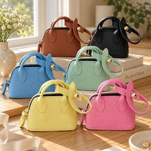 May include: A collection of six miniature handbags in brown, black, blue, mint green, yellow, and pink. Each small bag features a textured finish, a top handle, a zipper closure, and a decorative side charm with a gold-tone metal stud.