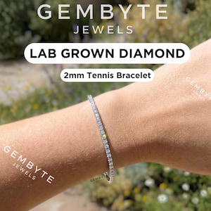 Pode incluir: Um close-up de um pulso usando uma pulseira de tênis de 2 mm. A pulseira é feita de pequenas pedras redondas e transparentes. O texto "LAB GROWN DIAMOND" e "2mm Tennis Bracelet" são visíveis. A marca "GEMBYTE JEWELS" também é visível.