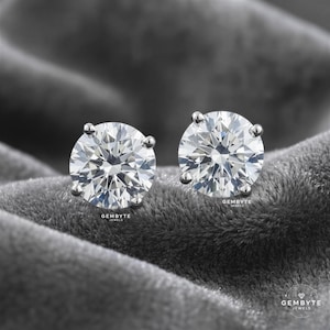two large, clear diamonds set in silver earrings, resting on a textured gray surface.