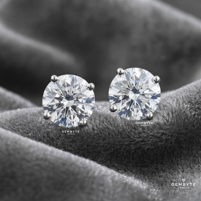 two large, clear diamonds set in silver earrings, resting on a textured gray surface.