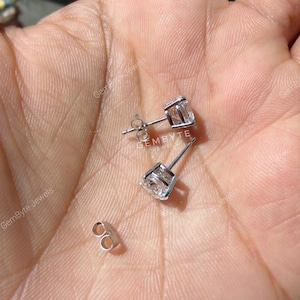 A hand holding a pair of silver earrings with clear gemstones.