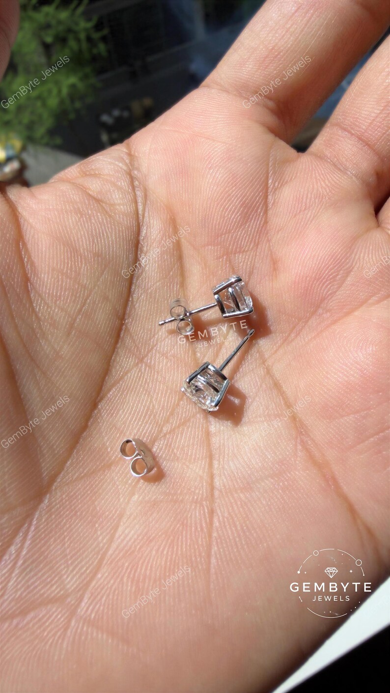 A hand holding a pair of silver earrings with clear gemstones.