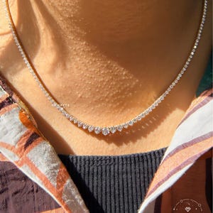 A close-up view of a woman's neck and chest area, featuring a delicate necklace with a row of small diamonds.