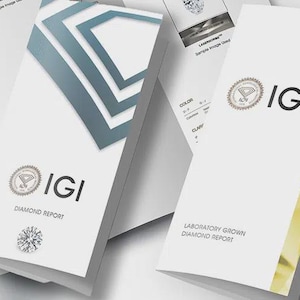May include: Two white IGI diamond report booklets are displayed. One features a blue geometric diamond graphic and the text "IGI DIAMOND REPORT," while the other shows the IGI logo and "LABORATORY GROWN DIAMOND REPORT" with a gold-toned side accent.