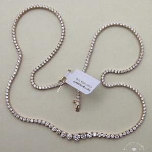 a gold necklace with numerous small diamonds arranged in a row, and a white tag attached to it.