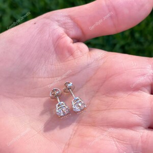 A close-up image of a person's hand holding a pair of diamond earrings.