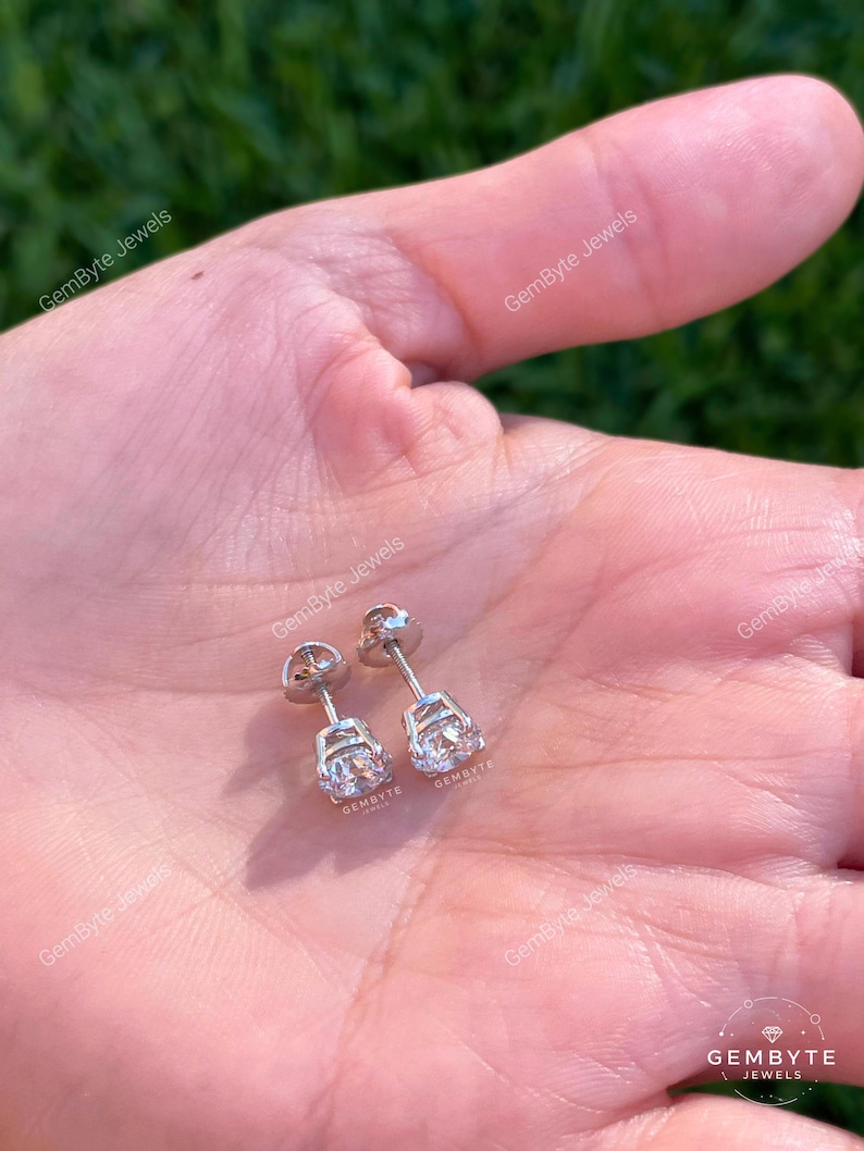 A close-up image of a person's hand holding a pair of diamond earrings.