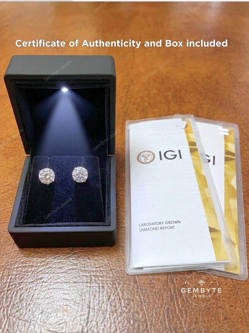a pair of diamond earrings in a black jewelry box, accompanied by a certificate of authenticity and a box containing a laboratory grown diamond report.