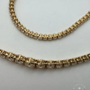 A close-up view of a gold necklace with numerous small diamonds set in the center.