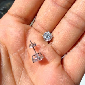 A close-up image of a person's hand holding a small diamond earring and a larger diamond earring.