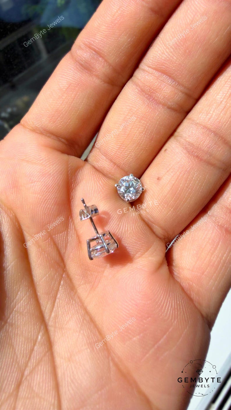 A close-up image of a person's hand holding a small diamond earring and a larger diamond earring.