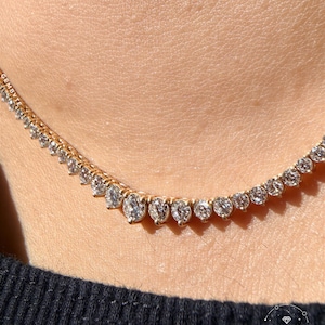 A close-up view of a delicate gold necklace with numerous small diamonds set in a row, worn around the neck of a person.