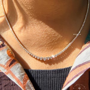 A close-up of a woman's neck wearing a diamond necklace with a row of diamonds on the chain.
