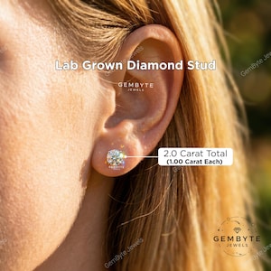 a close-up of a person's ear with a lab-grown diamond stud. The earring has a 2.0 carat total (1.00 carat each) and is labeled as a lab-grown diamond stud from Gembyte Jewels.
