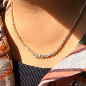 A close-up view of a person's neck and chest area wearing a gold necklace with a row of small diamonds.