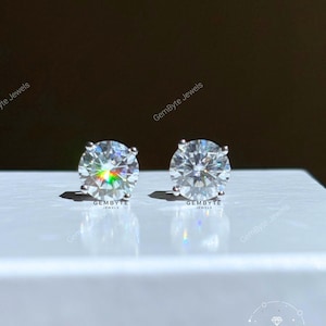 two large, clear, and sparkling diamond earrings placed on a white surface.