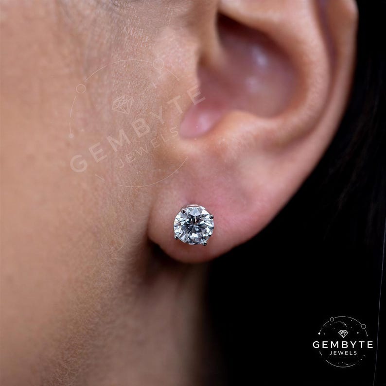 A close-up of a person's ear with a large, clear diamond earring in the earlobe.