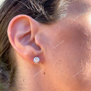 A close-up of a person's ear with a diamond earring in the earlobe.