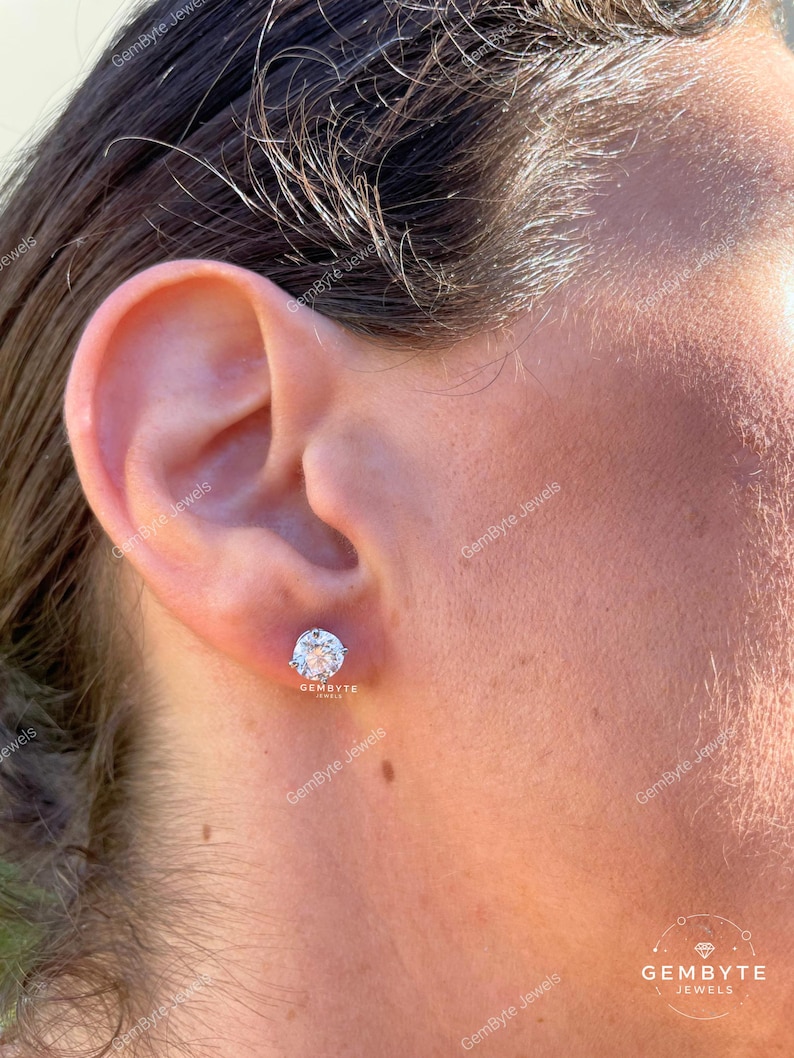 A close-up of a person's ear with a diamond earring in the earlobe.