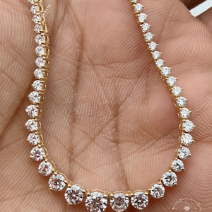 A close-up image of a gold necklace with a row of diamonds on it, held in someone's hand.